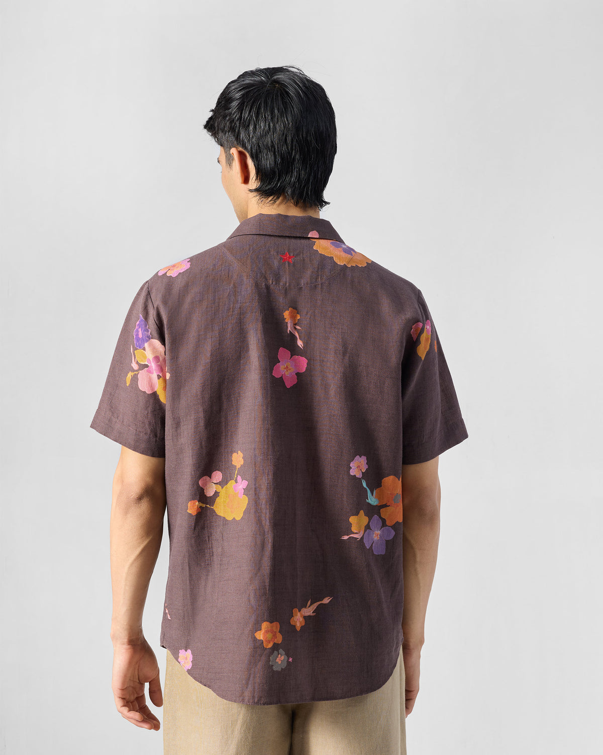 Back of a brown Mistari shirt with floral print and a red star.