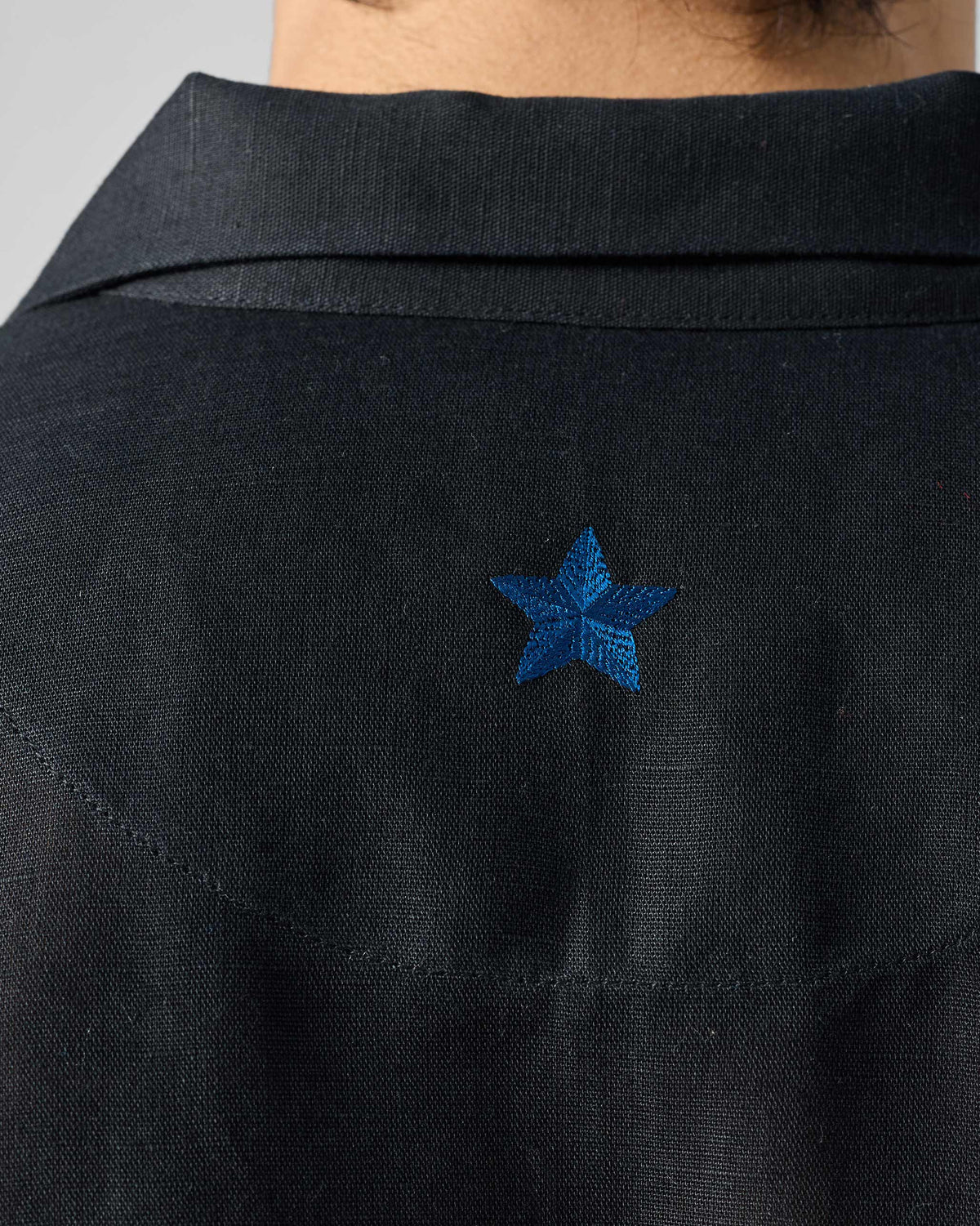 Close-up of a blue embroidered star on the back yoke of a black Delta shirt.