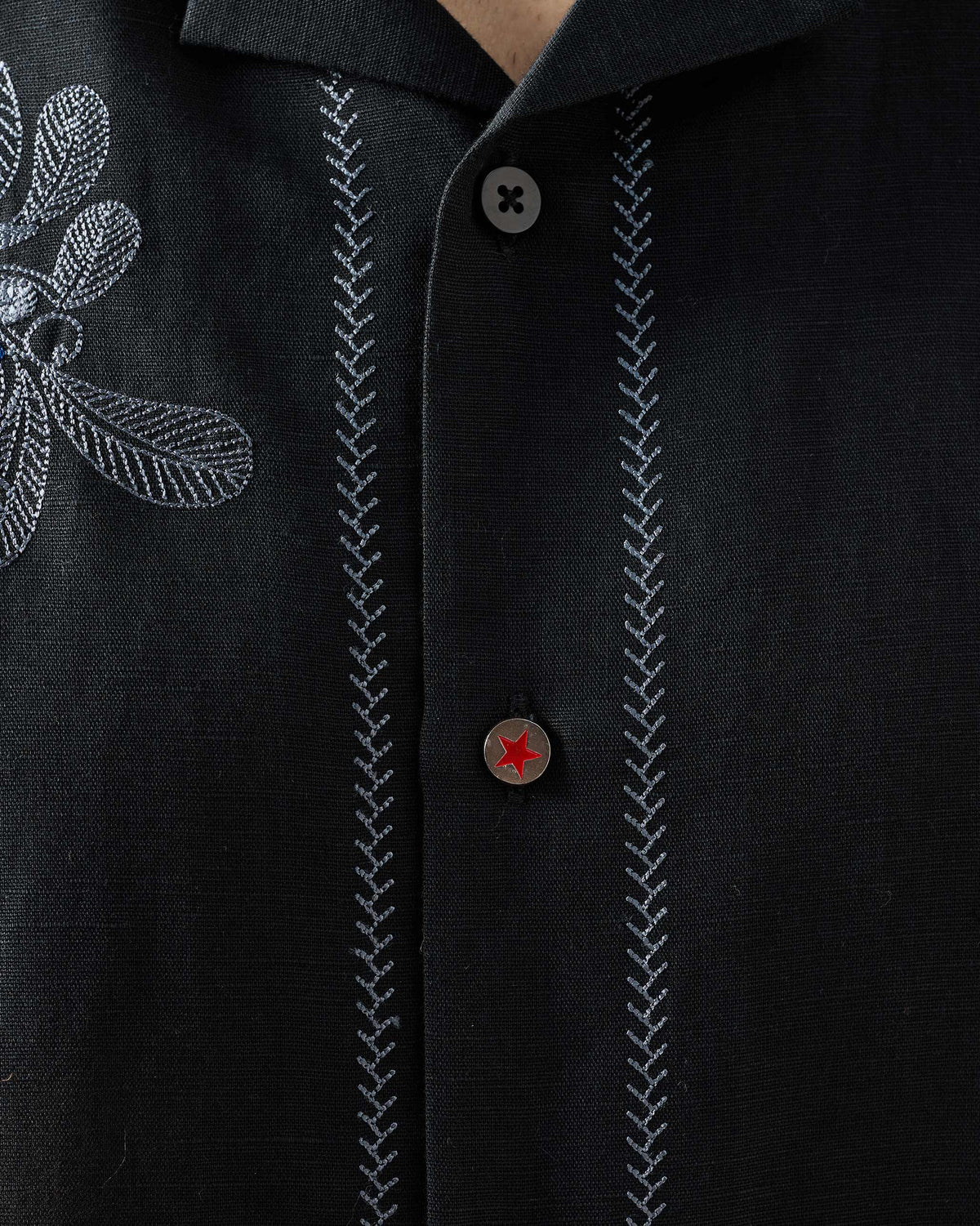 Close-up of a red star button and contrast placket stitching on a black Delta shirt.