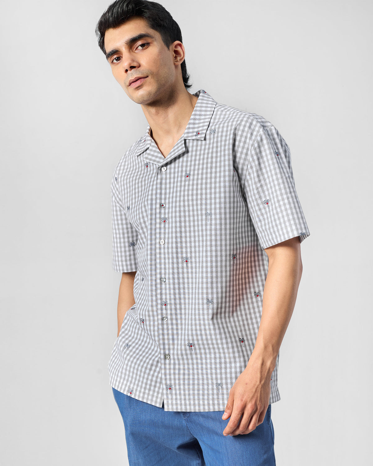 Person wearing a charcoal and white gingham Bena shirt with palm tree embroidery.