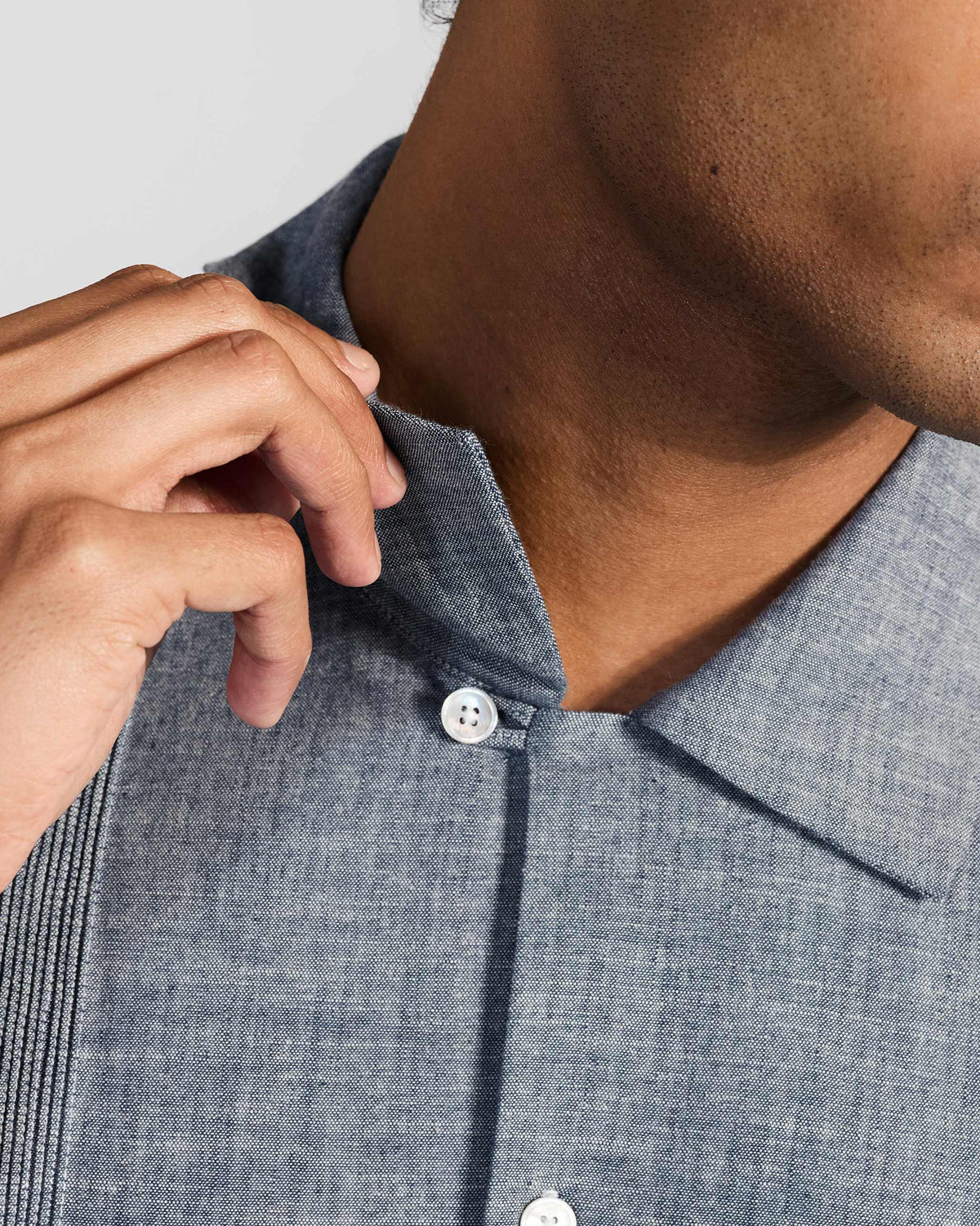 Close-up of a hand adjusting the pointed collar on an indigo textured shirt with a white button.