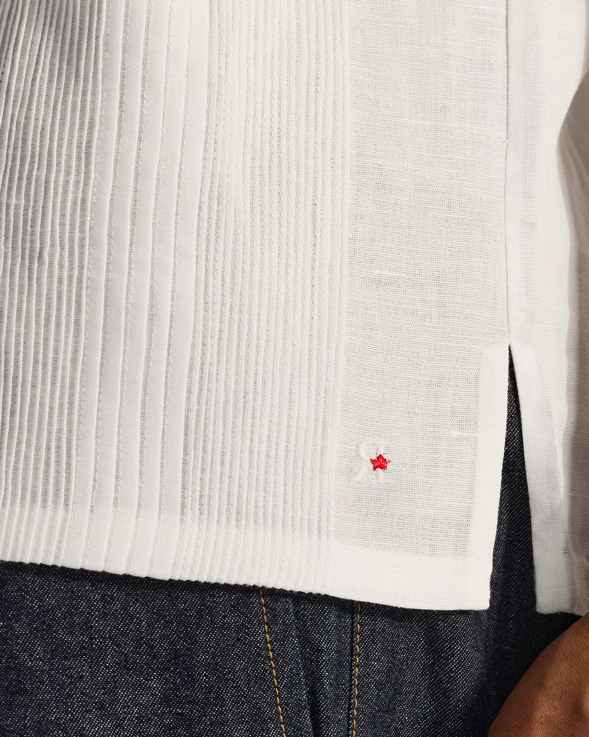 Close-up of pintucks and a red star at the hem of a white Egret shirt.