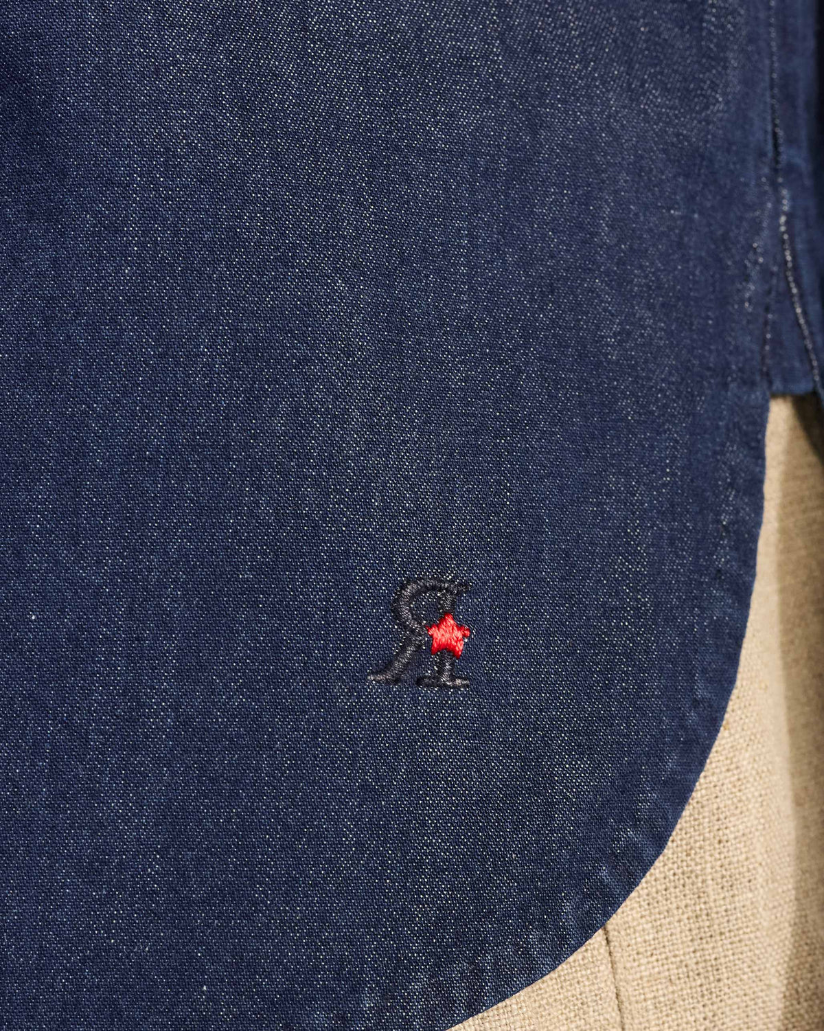 Close-up of a red star logo near the hem of an indigo Loris shirt.