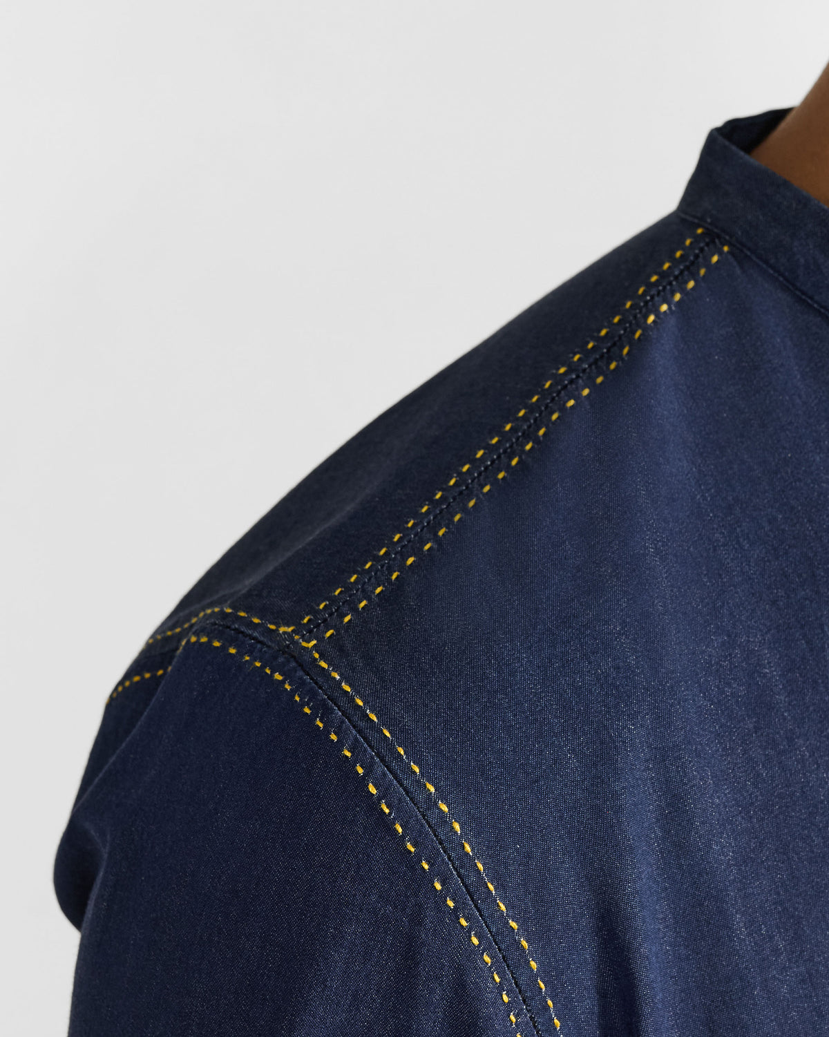 Close-up of yellow stitching on the shoulder of an indigo Loris shirt.
