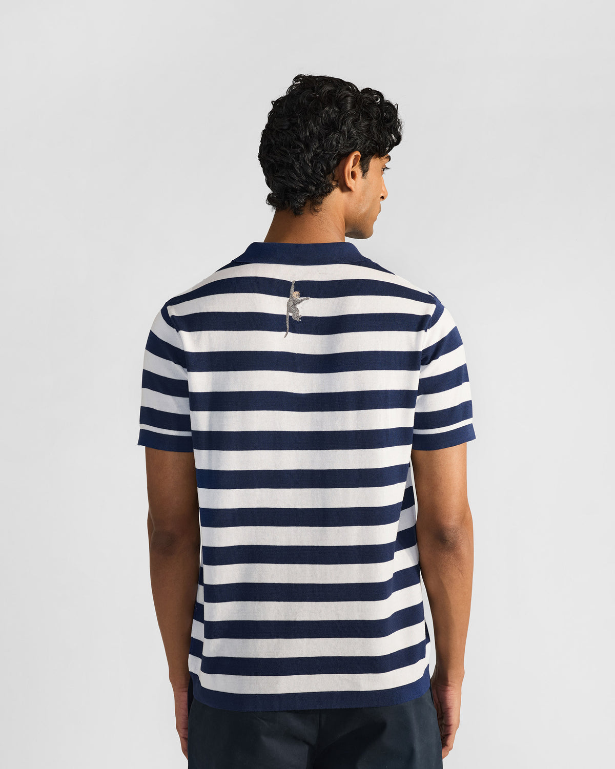 Back of a navy-and-white striped polo with an embroidered macaque below the collar.