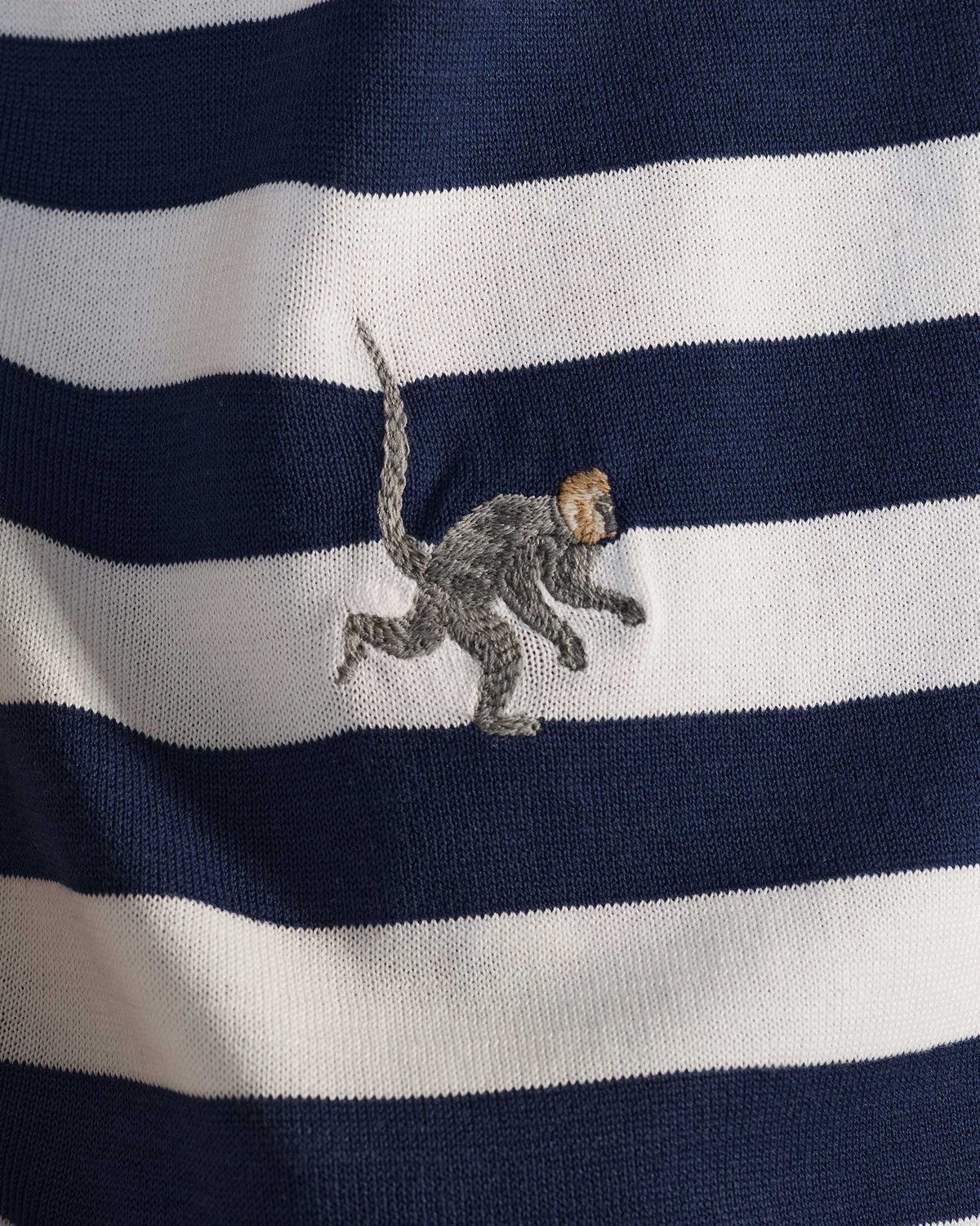 Close-up of an embroidered macaque on a navy-and-white striped polo.