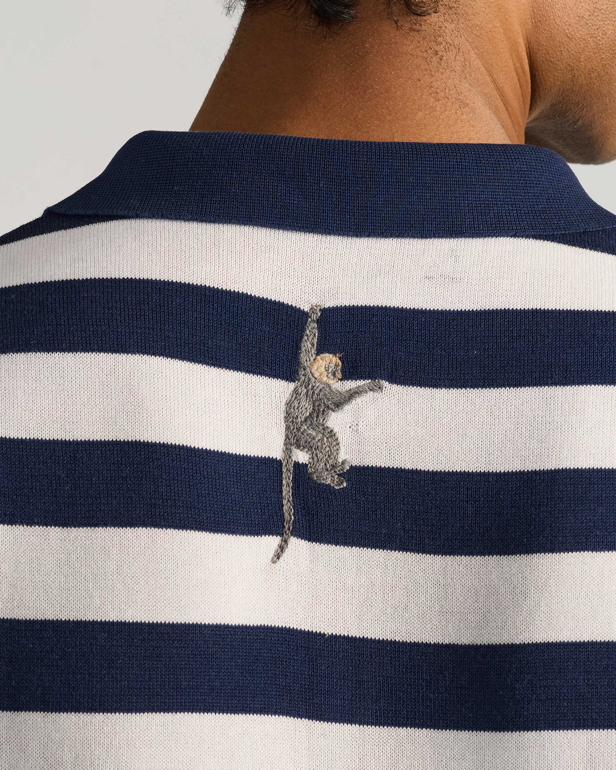 Close-up of the navy collar and back macaque embroidery on a striped polo.