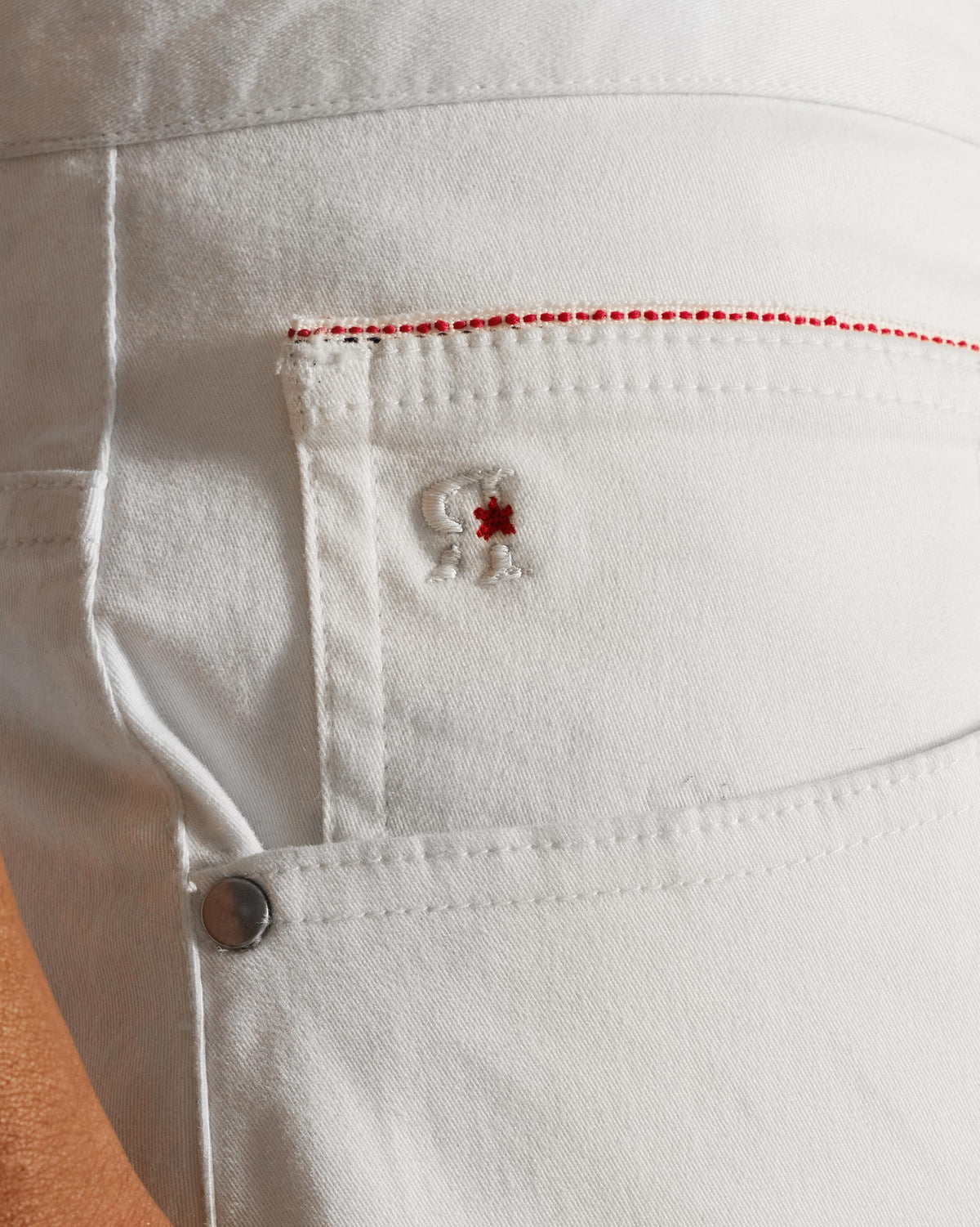 Close-up of an off-white Serow jodhpur pant pocket with red stitching.