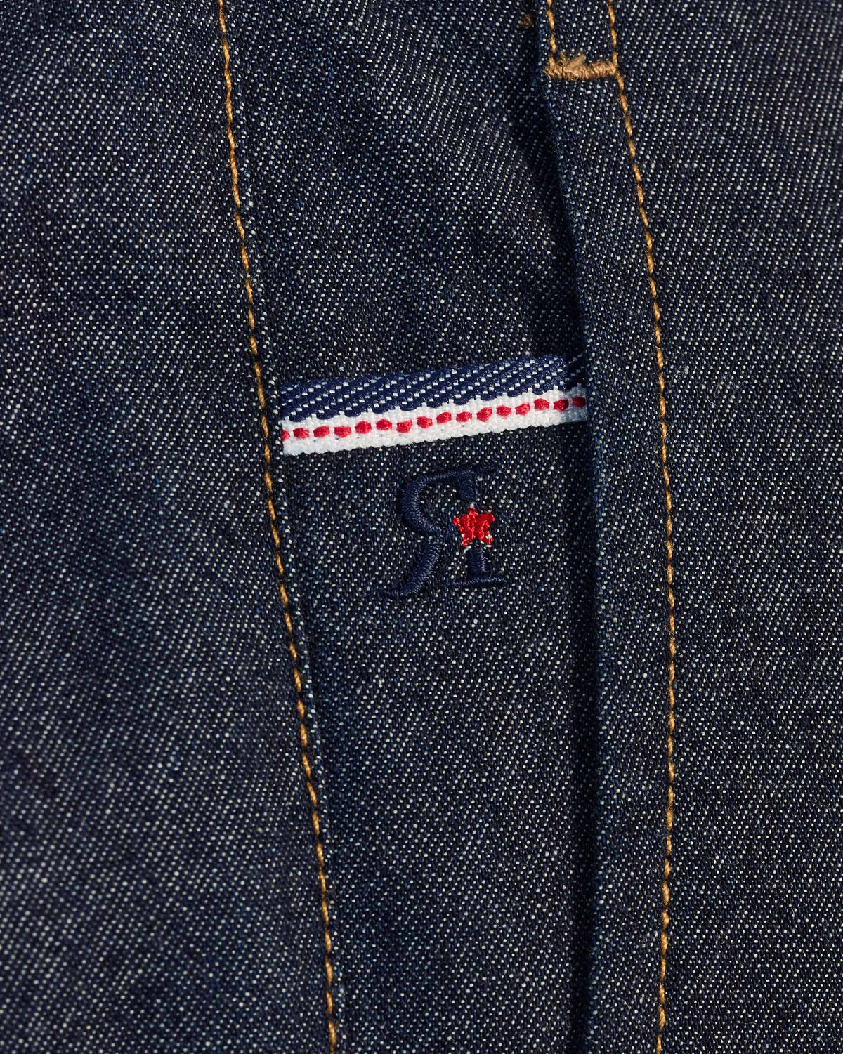 Close-up of a striped tape and red star detail on denim Thrush Trousers.