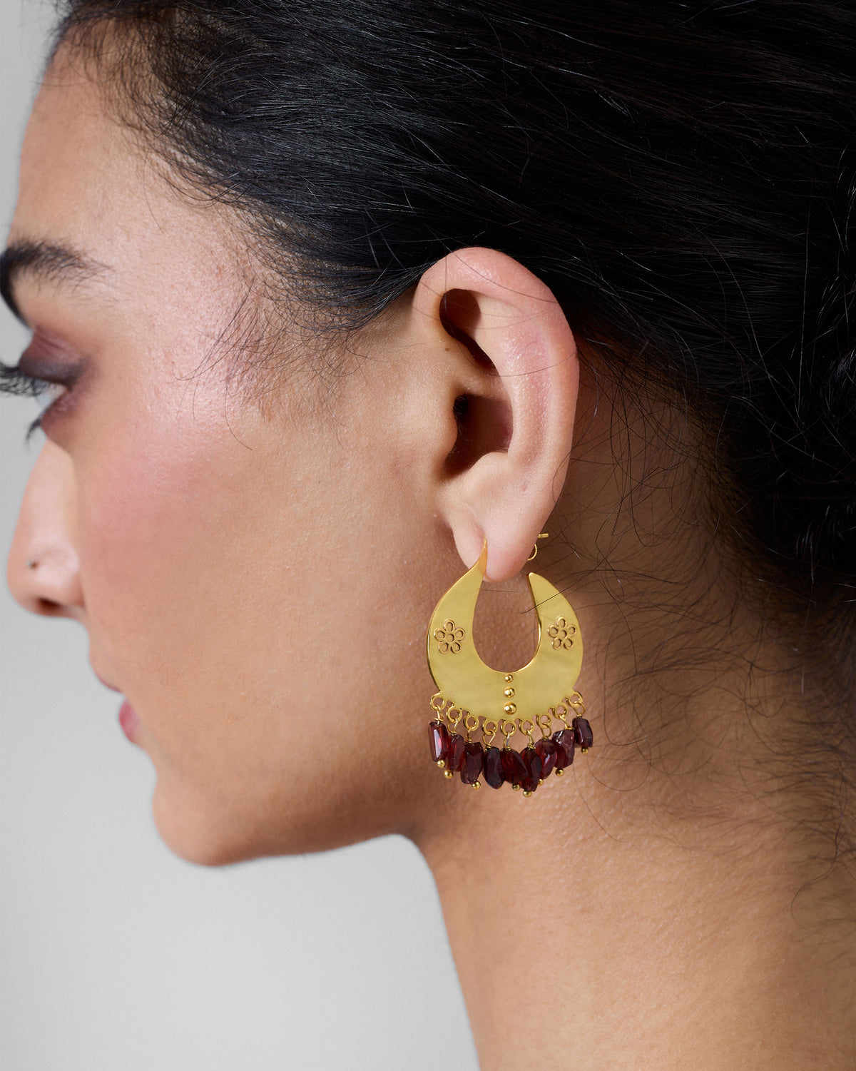 Side profile of gold Anaar earrings with a red glass bead fringe on a person.