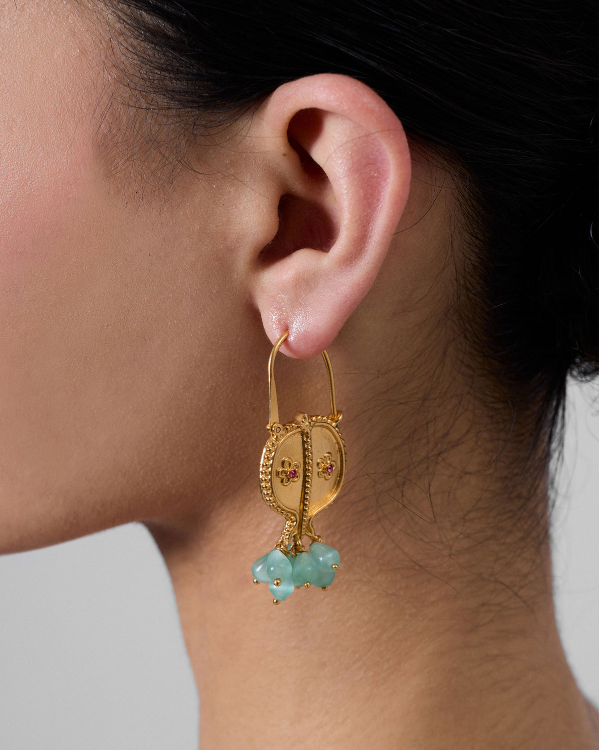 Side profile of gold Anaar balis with floral red stones and blue beads on a person.