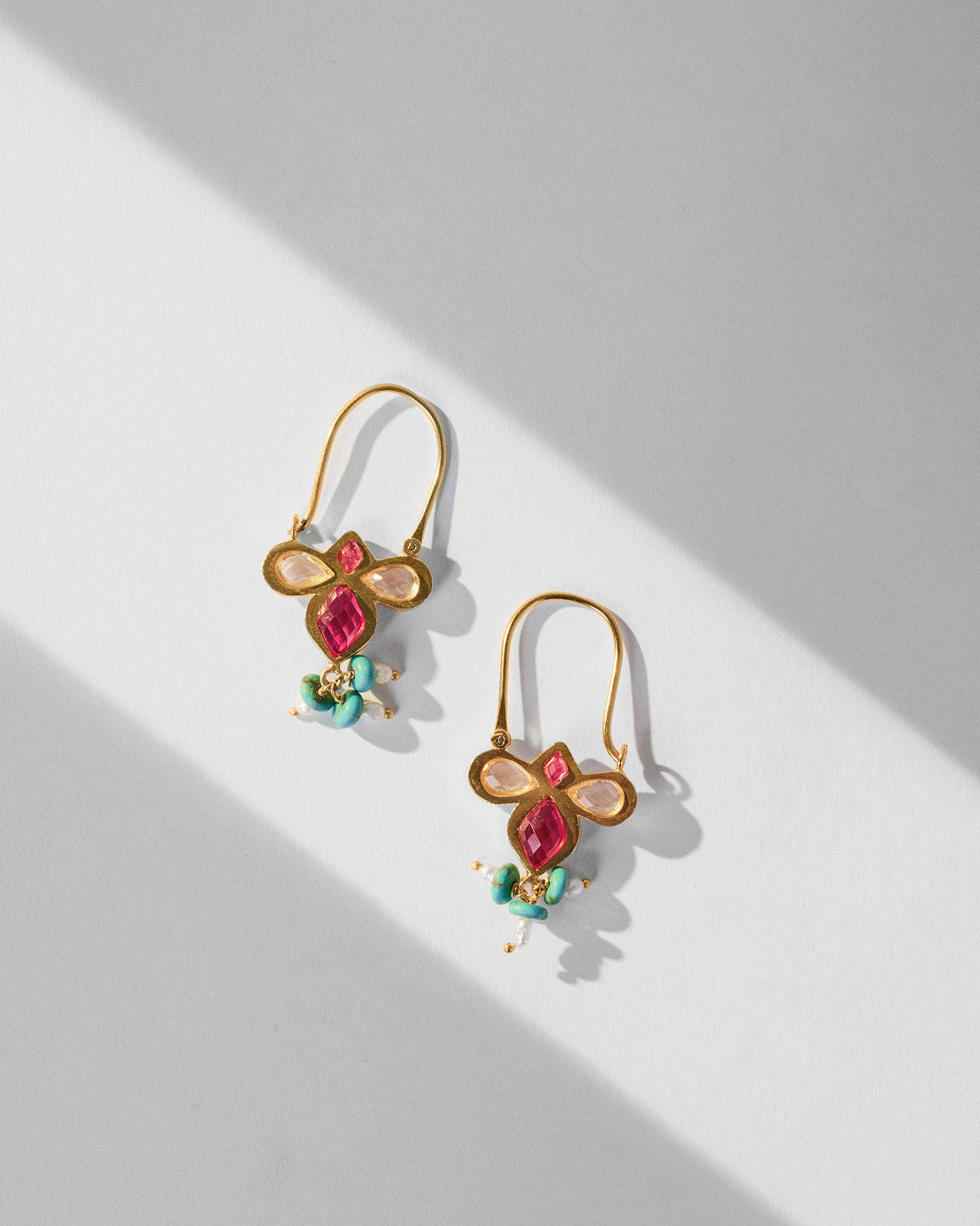 Pair of gold doli earrings with pink glass and turquoise tassels laid flat.