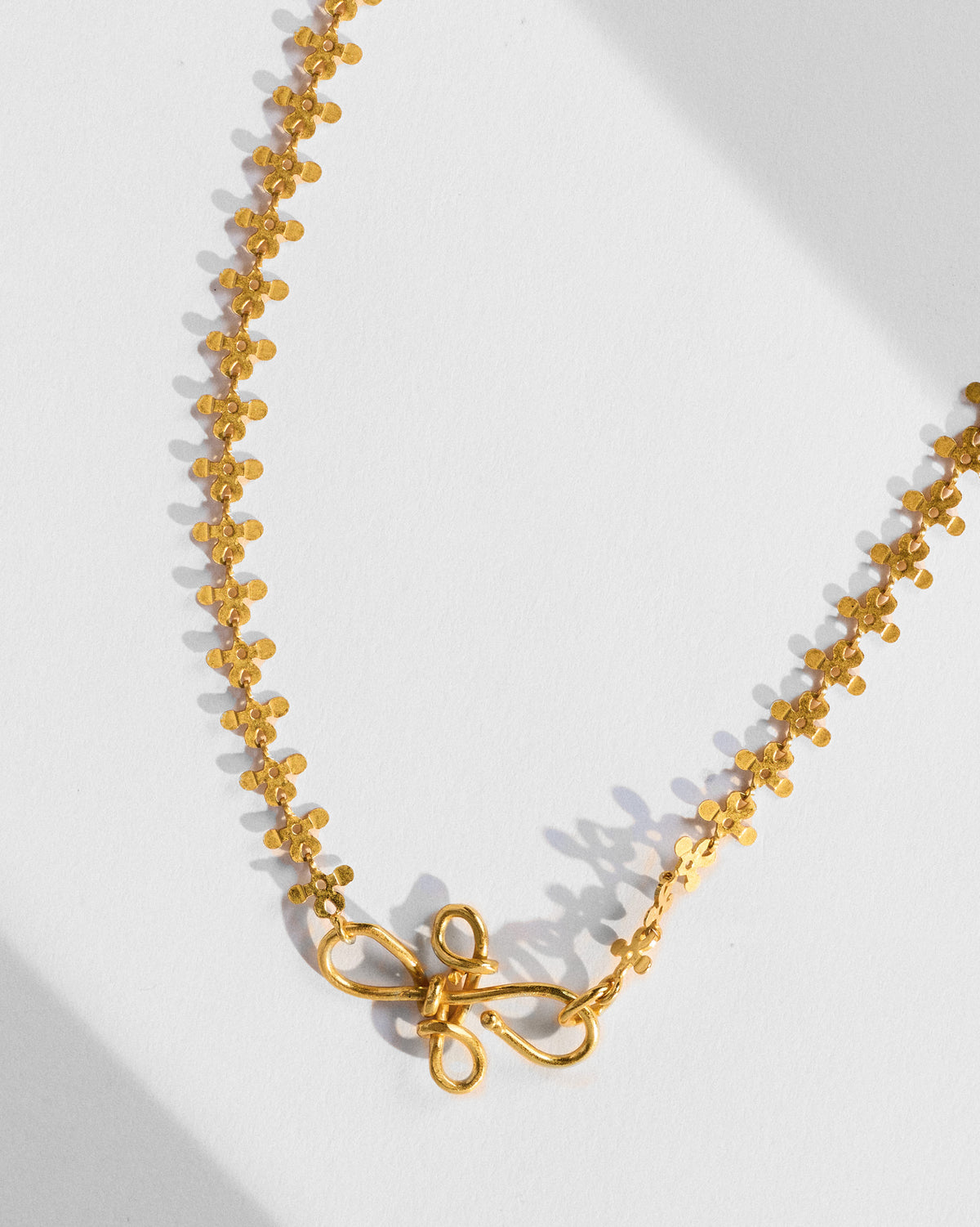 Gold Milni necklace with an infinity knot clasp and floral links.