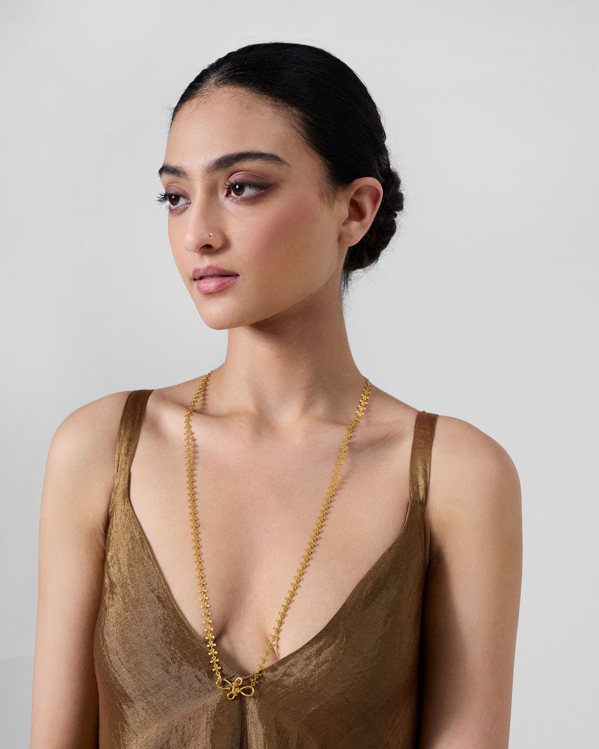 Gold Milni necklace worn long over a bronze V-neck top.