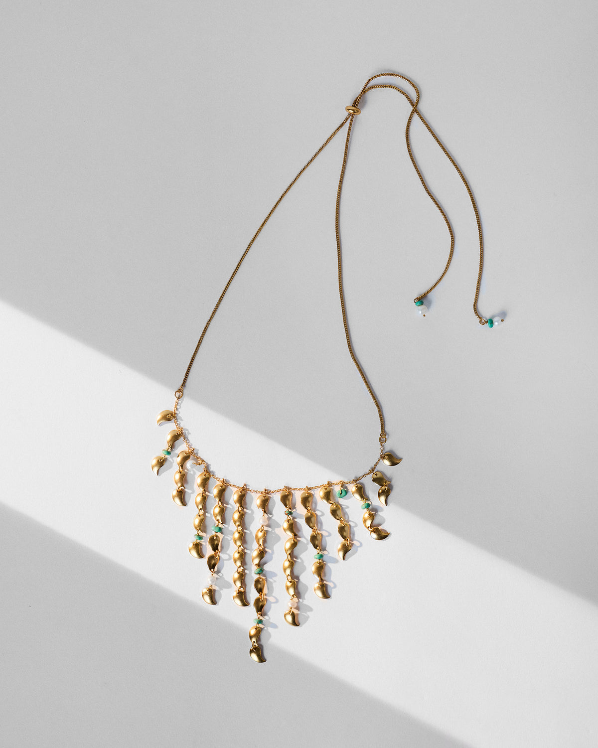 Gold Kairi necklace with a V-shaped fringe of mango charms and turquoise beads.