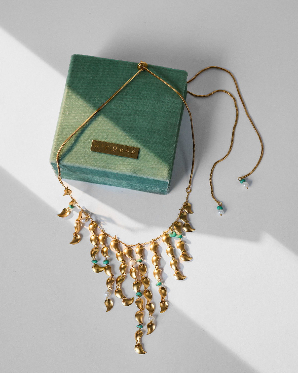 Gold Kairi necklace draped on a green Nicobar velvet gift box.