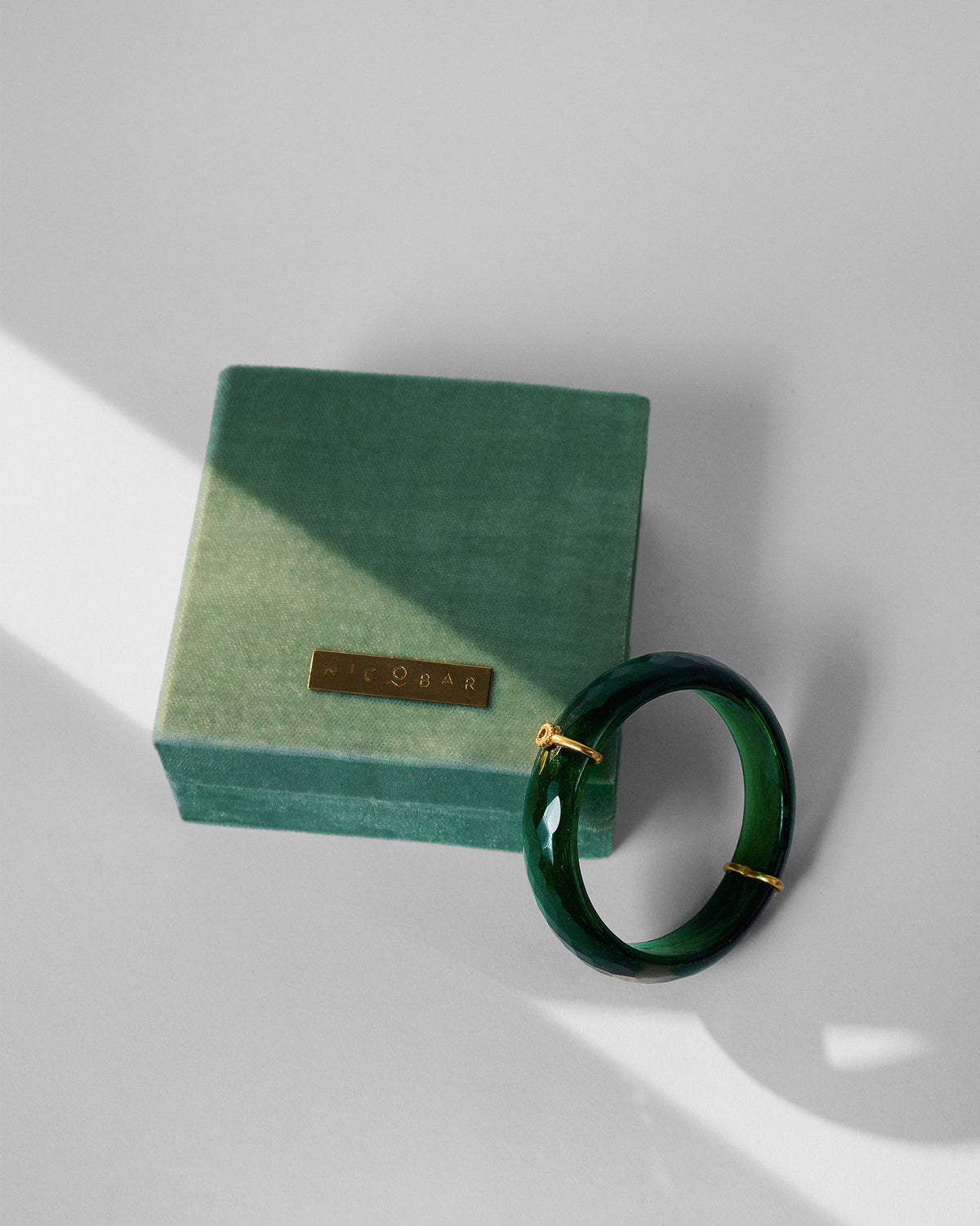 Green glass dhoop bangle beside a sage Nicobar velvet box.
