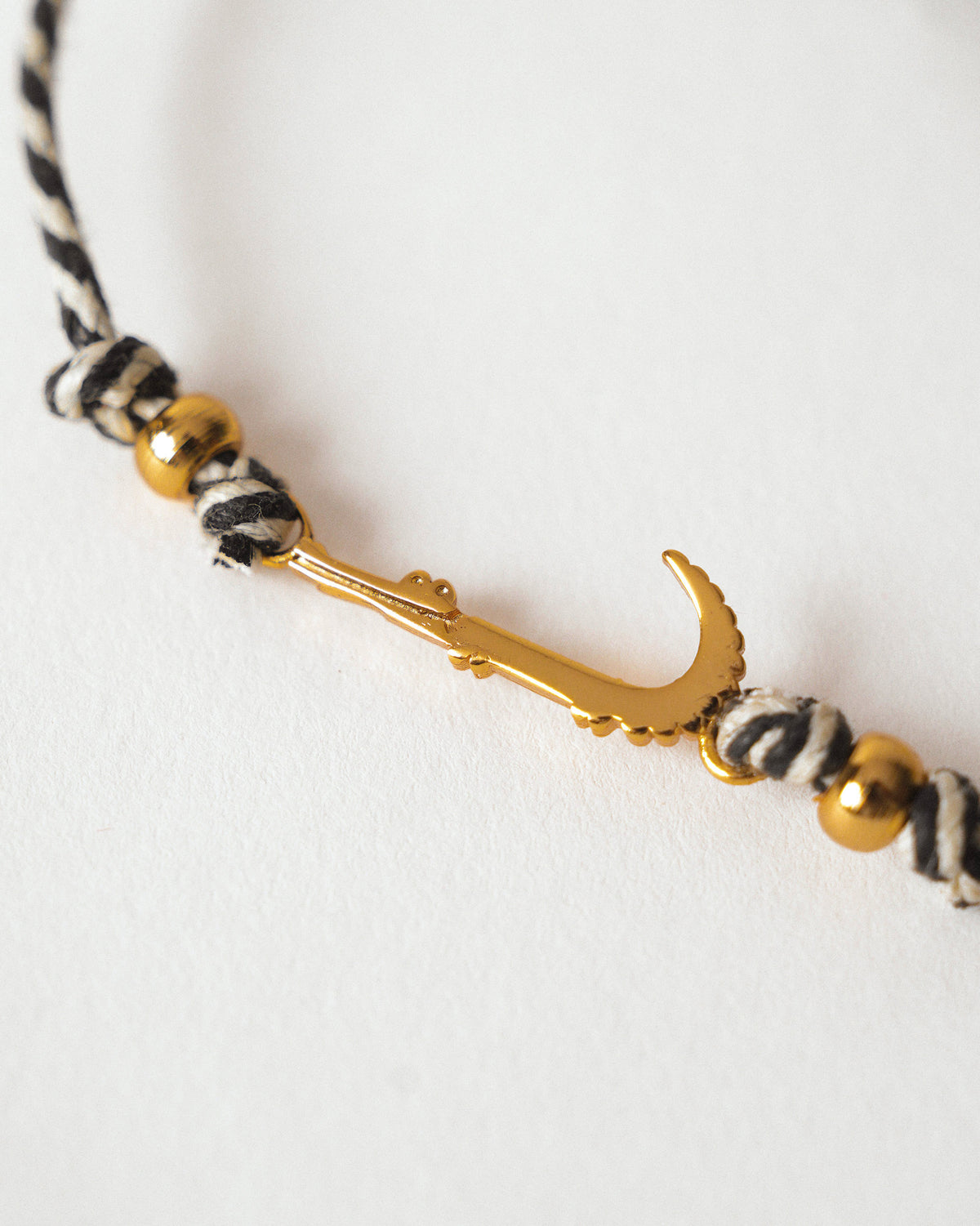 Close-up of Croc Rakhi showing a gold curved charm on black and white cord.