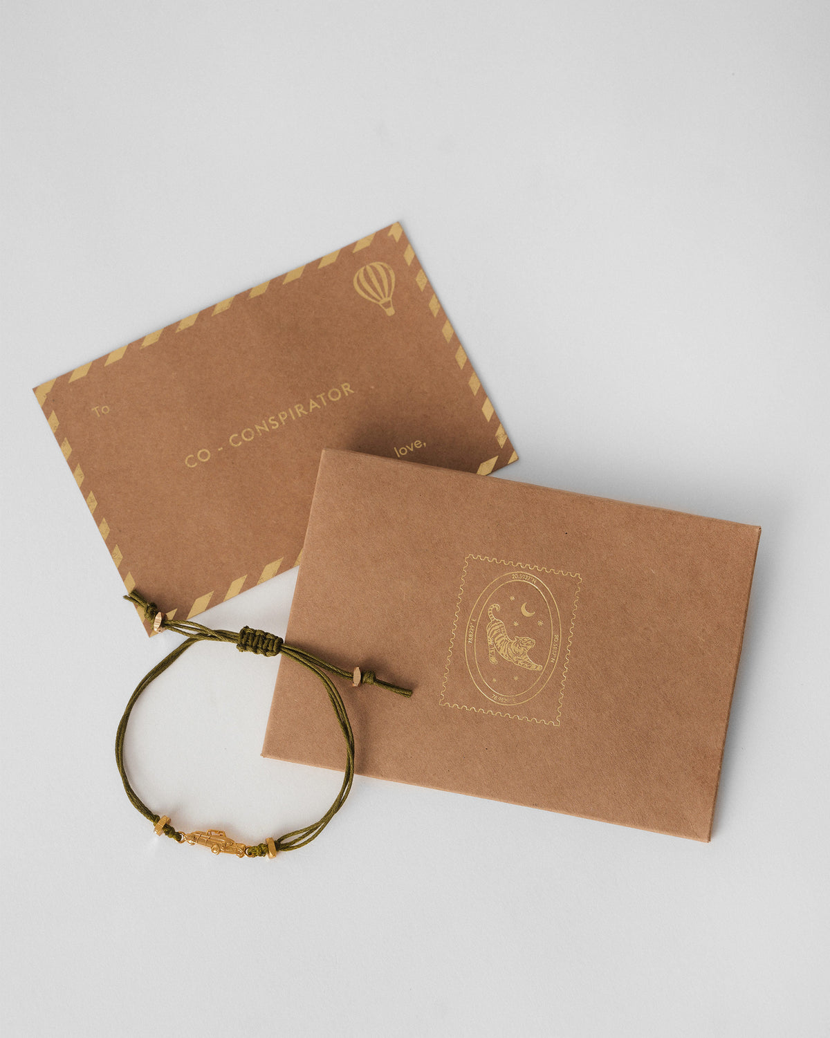 Vintage Car Rakhi in green laid beside kraft gift envelopes.