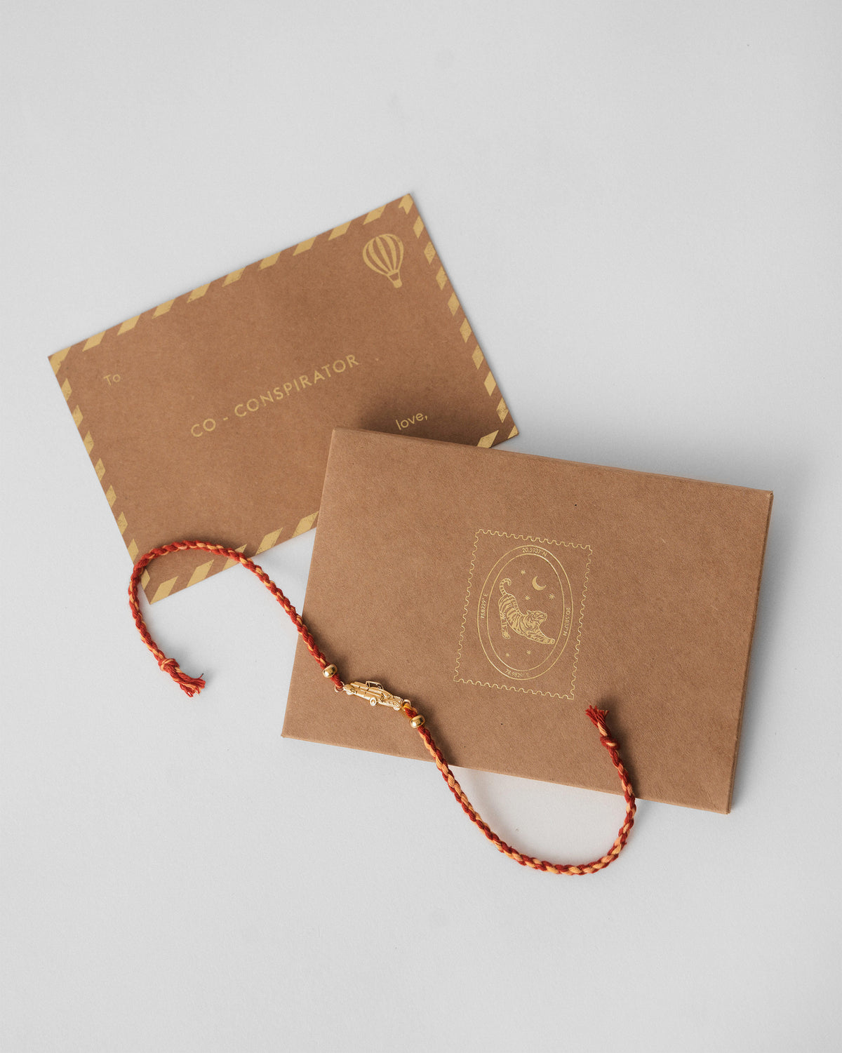 Vintage Car Rakhi in red laid beside kraft gift envelopes.