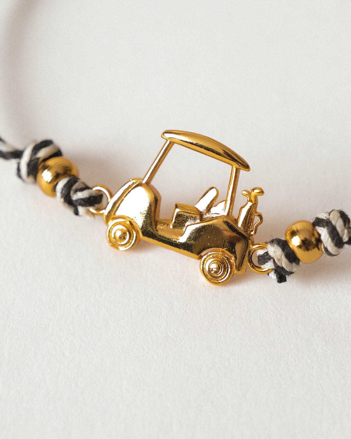 Close-up of a Golf Cart Rakhi with a gold golf cart charm on black and white thread.