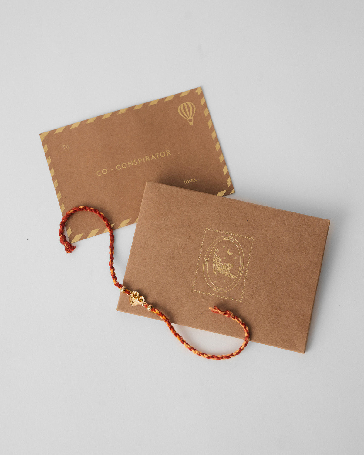 Dil Rakhi with a heart charm laid across brown kraft envelopes.