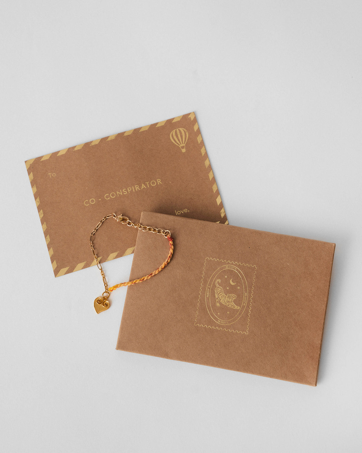 Dil Charmlet beside a kraft gift envelope and card.