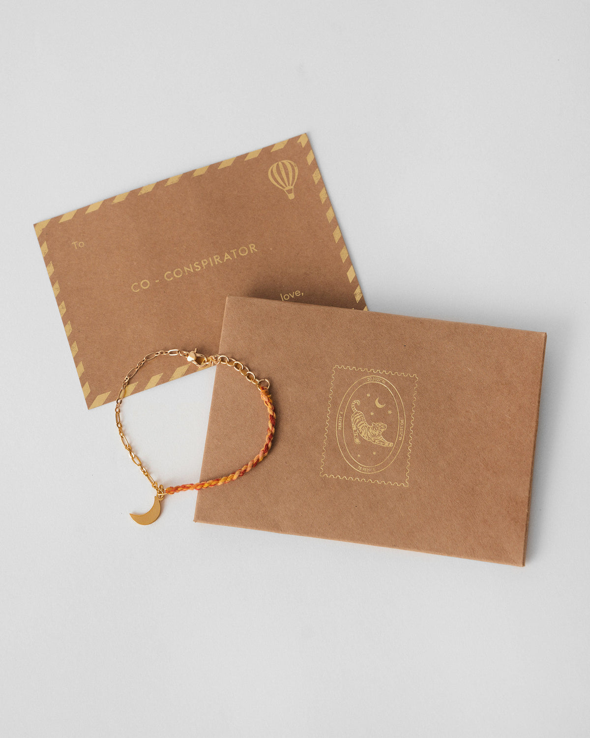 Crescent Charmlet laid beside a kraft envelope on a grey surface.