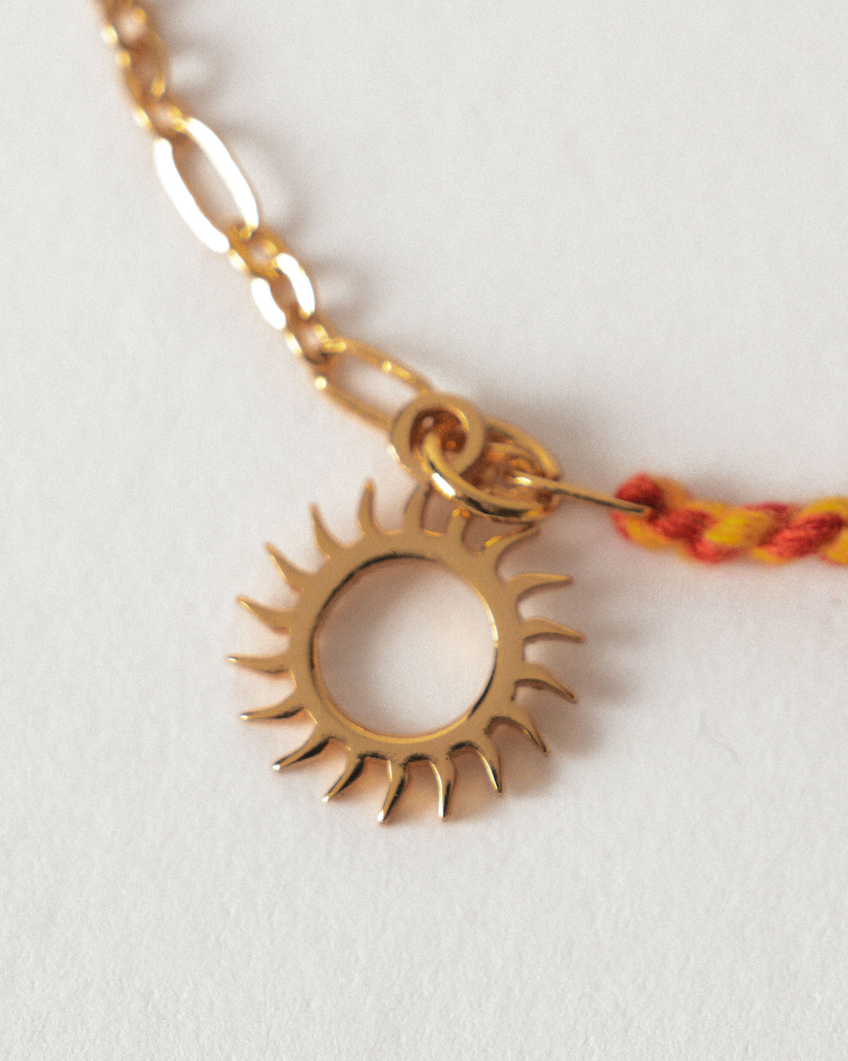 Close-up of gold Sun Charmlet showing its open sun-ray charm on a braided cord.