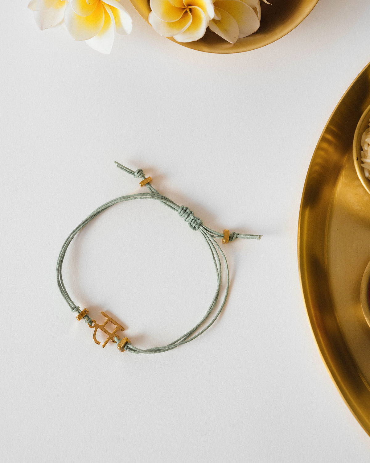 Alphabet S Rakhi laid flat with a gold letter charm on a green cord.