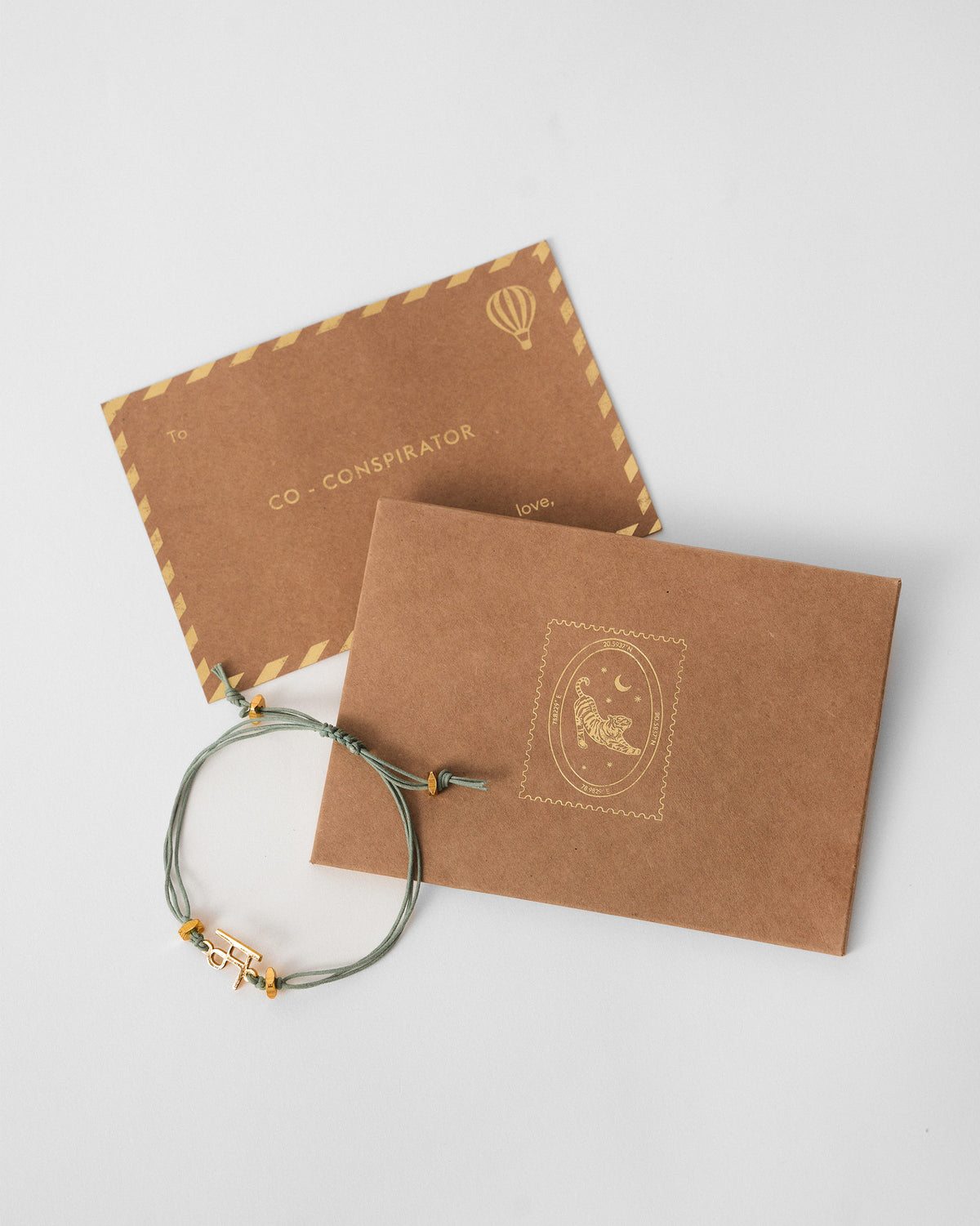 Alphabet M Rakhi beside a kraft envelope and card.