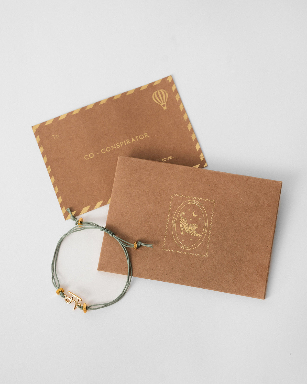 Alphabet M rakhi with a gold charm beside Nicobar gift cards.