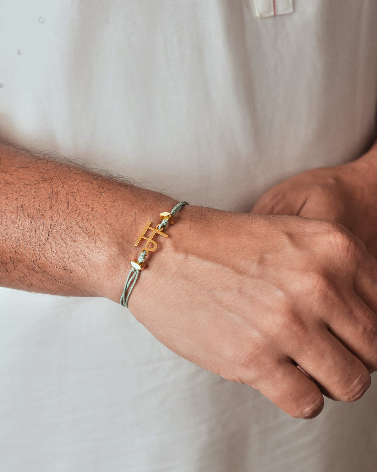 Person wearing Alphabet M Rakhi with a gold charm on the wrist.