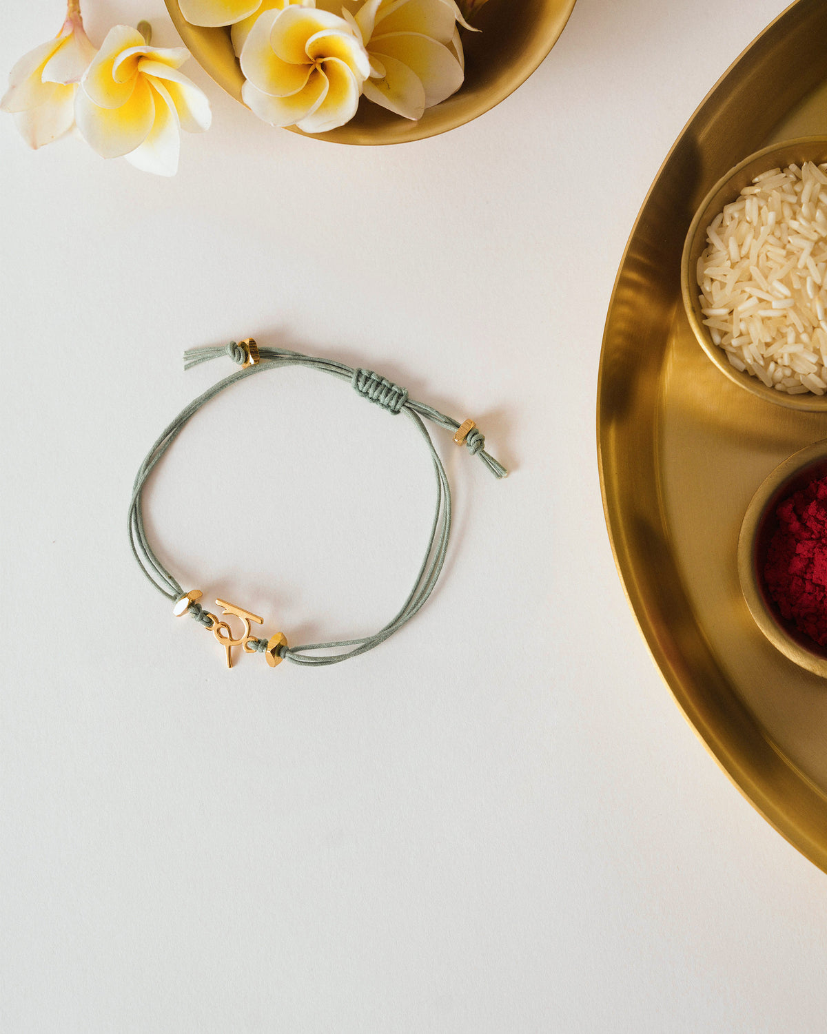 Alphabet R Rakhi laid flat with a gold letter charm on a green cord.