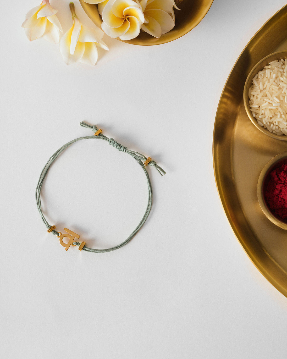 Alphabet V Rakhi with a gold charm on a pale green cord, lying on a white surface.