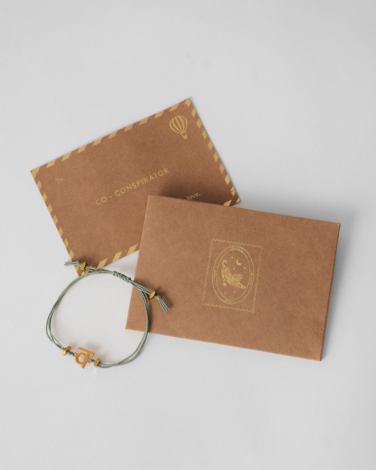 Alphabet V Rakhi with a gold charm, placed across a kraft envelope.