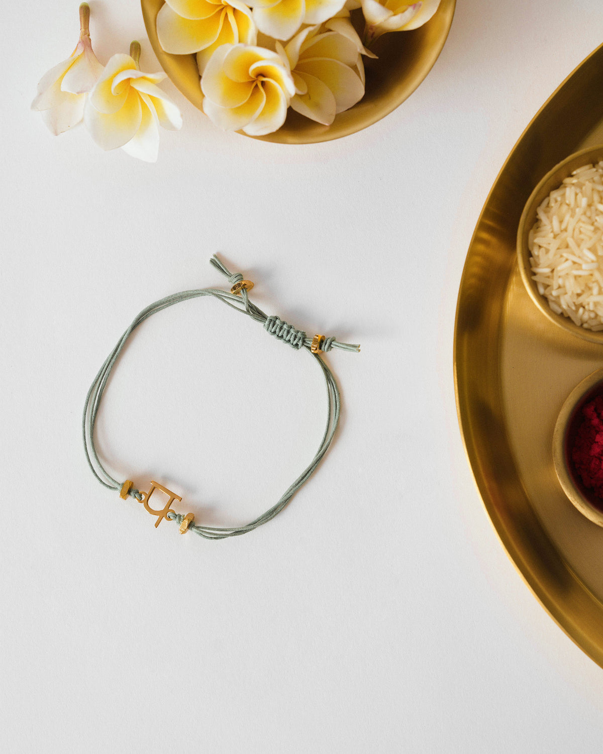 Alphabet P Rakhi with a gold charm on a pale green cord, lying on a white surface.