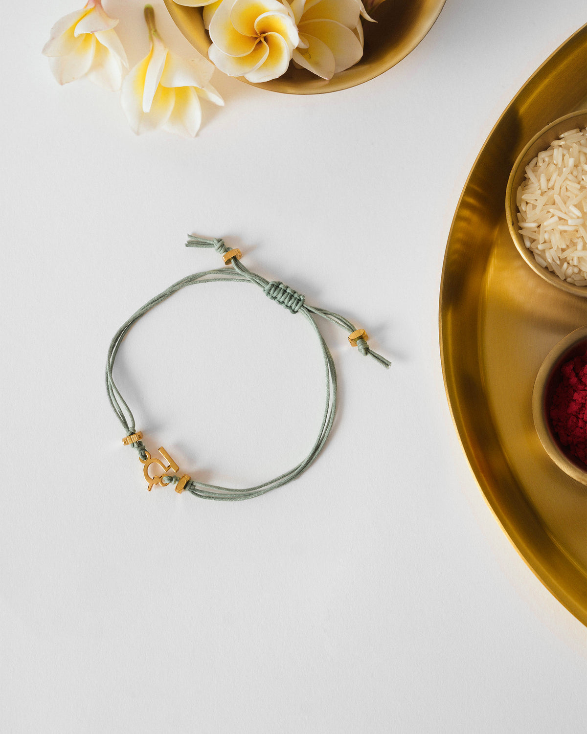 Alphabet D Rakhi with a sage green cord and gold charm, laid flat.