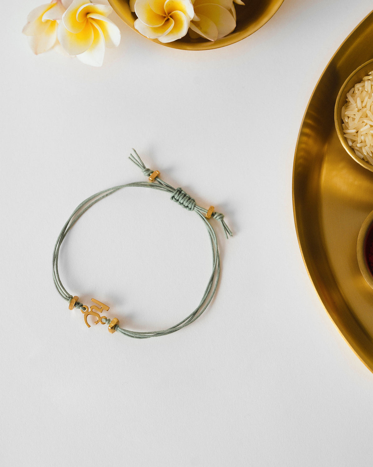 Alphabet H Rakhi with a sage green cord and gold charm, laid flat.
