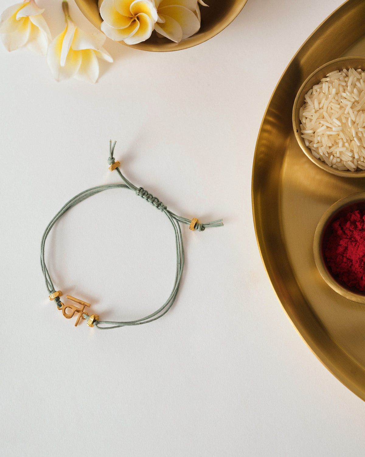 Alphabet N Rakhi with a sage green cord and gold charm, laid flat.