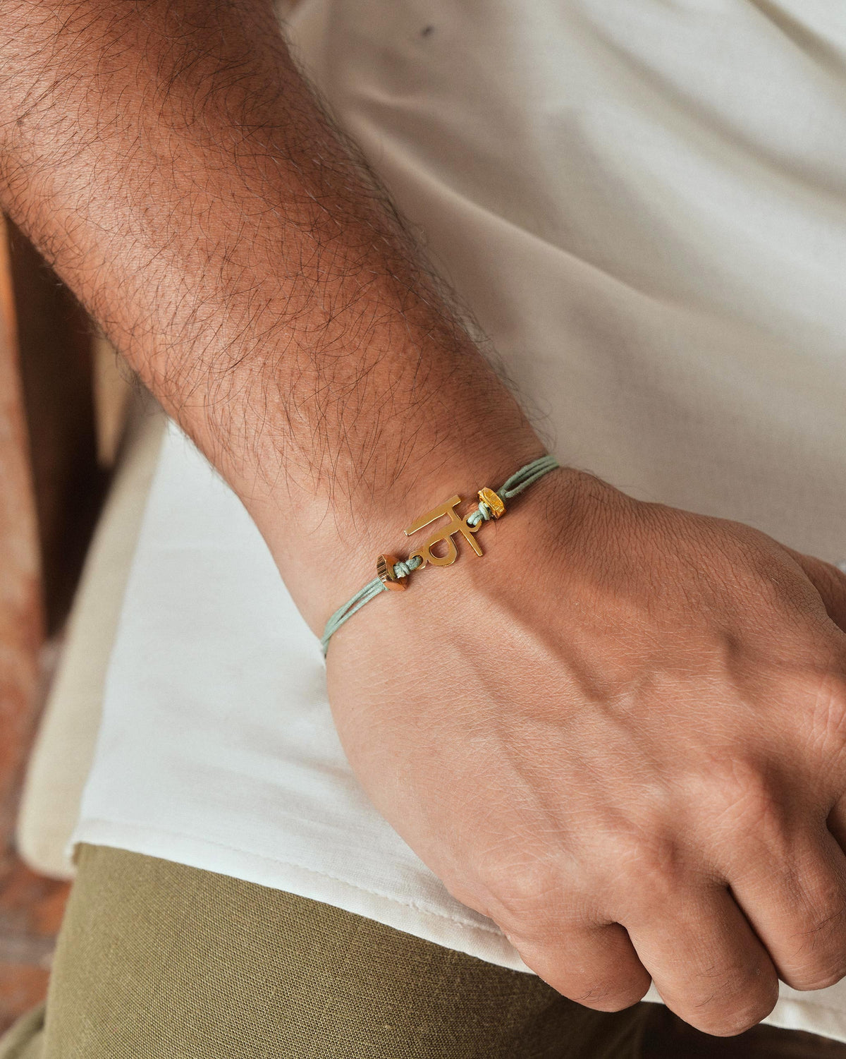 Person wearing Alphabet N Rakhi with a gold charm on the wrist.