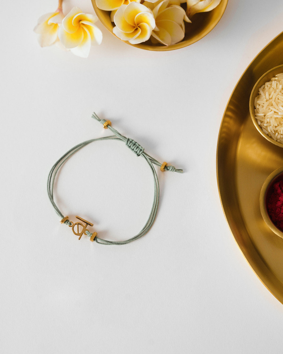 Alphabet B Rakhi with a sage green cord and gold charm, laid flat.