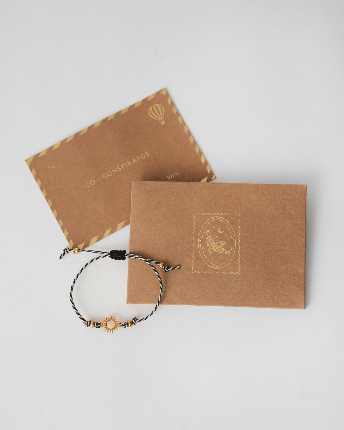 Surya Rakhi in charcoal and white stripes laid over a kraft envelope.