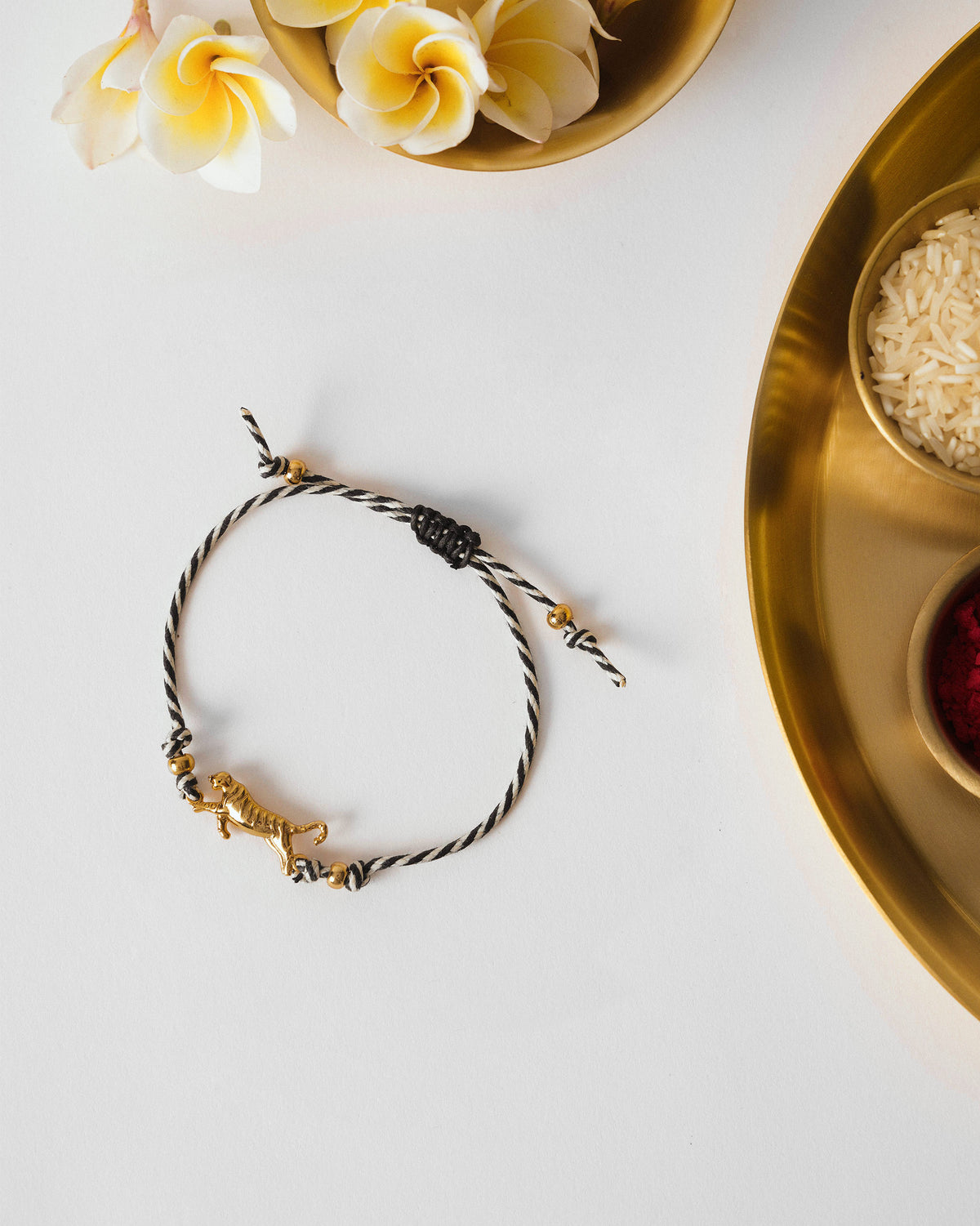 Tiger Rakhi in charcoal and white stripes with a gold tiger charm, laid flat.