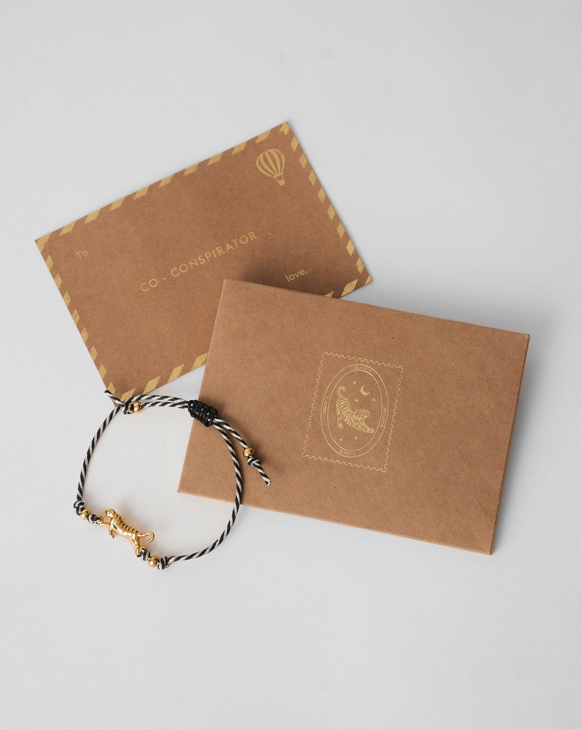 Tiger Rakhi with a gold tiger charm laid over a kraft envelope.