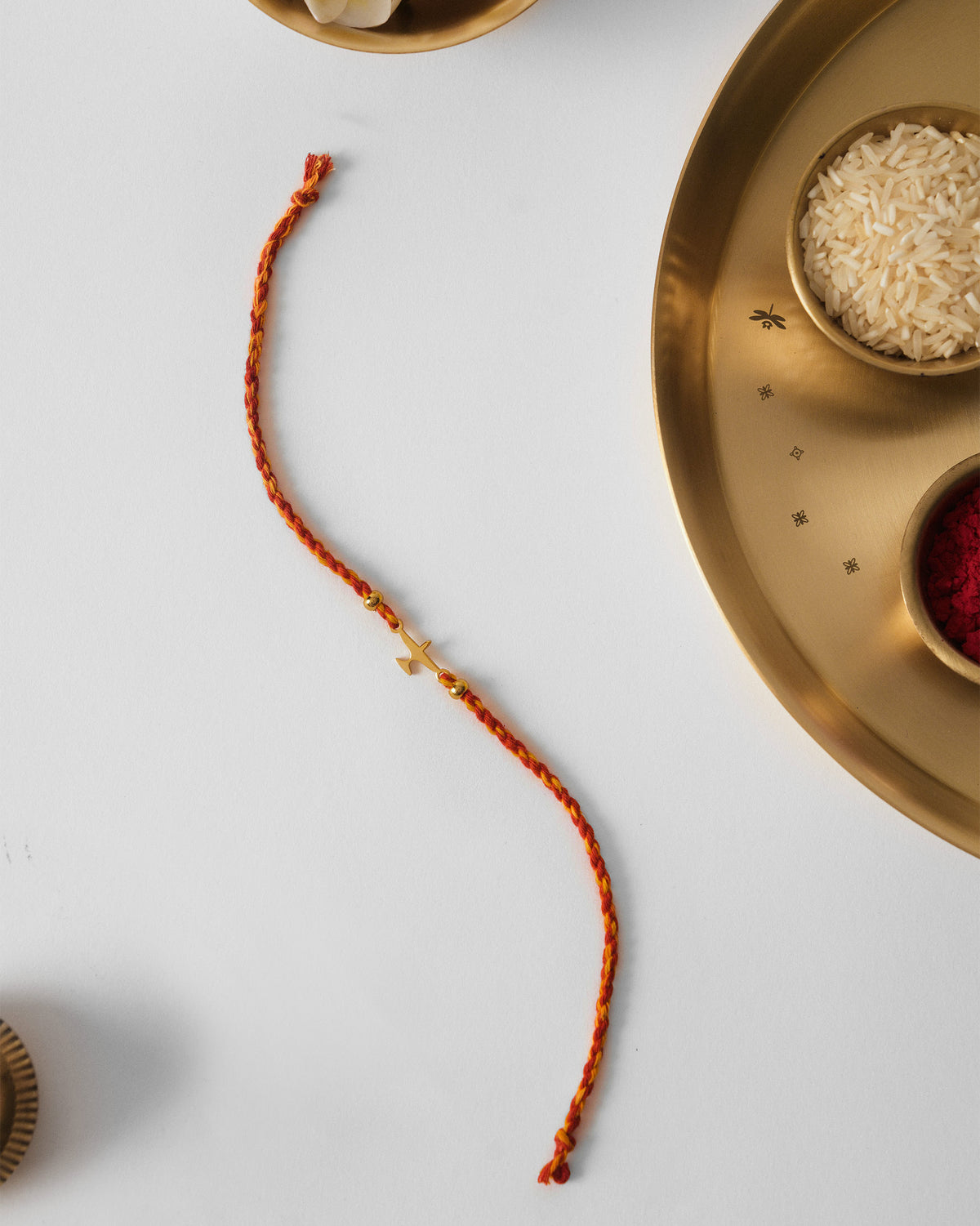 Airplane Rakhi laid in a curve on white, with a gold charm on red cord.