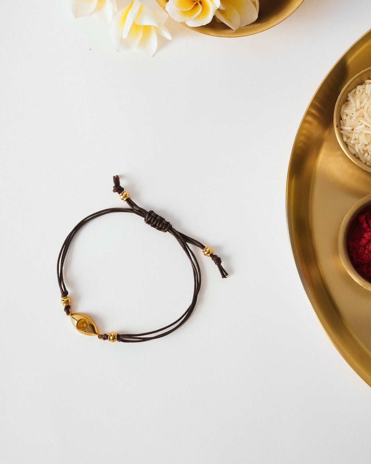 Brown Evil Eye Rakhi with a gold charm laid flat.