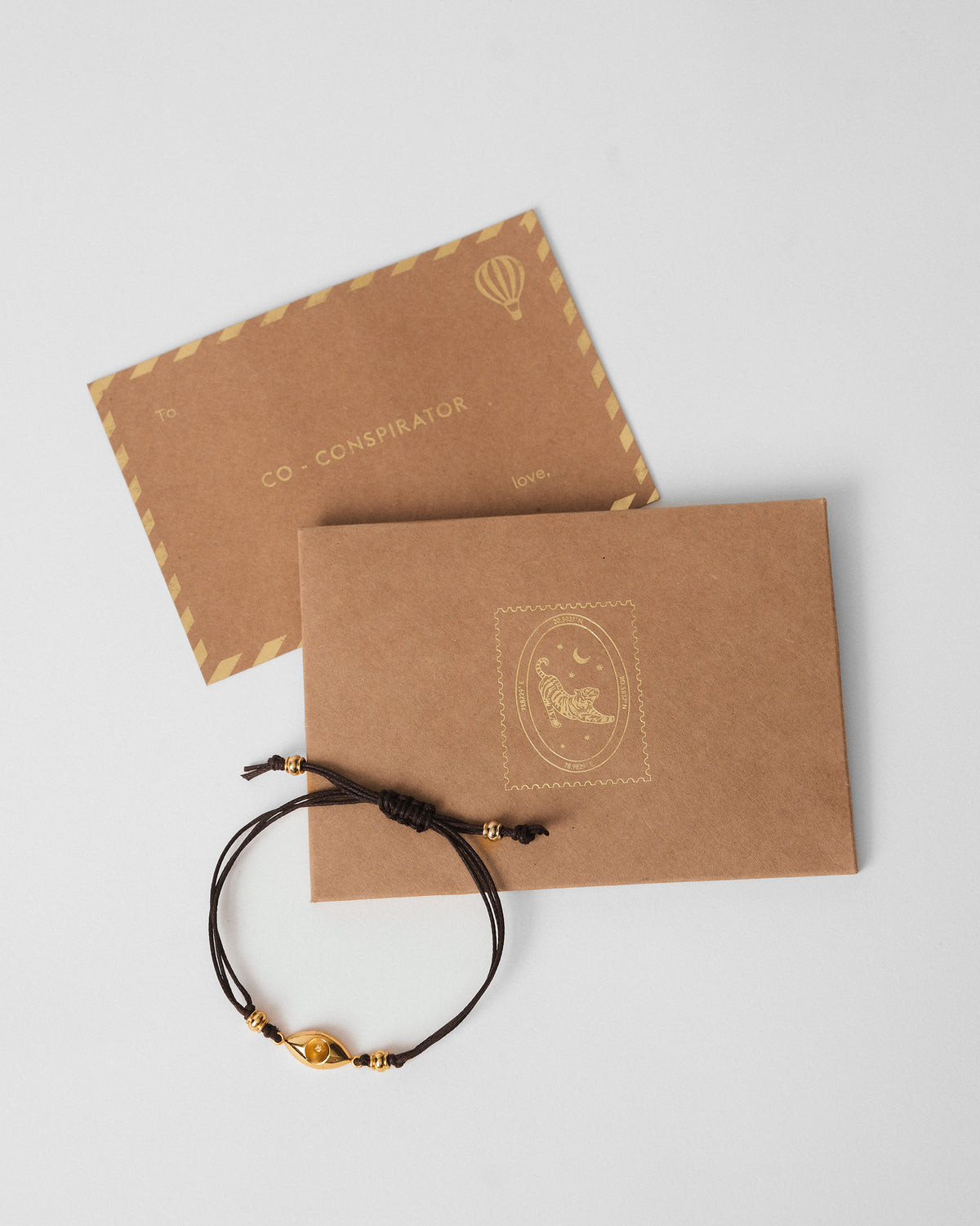 Brown Evil Eye Rakhi beside a kraft gift envelope and card.