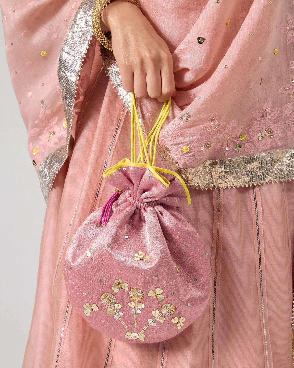 Light pink Meher potli with floral embroidery held by the drawstrings.