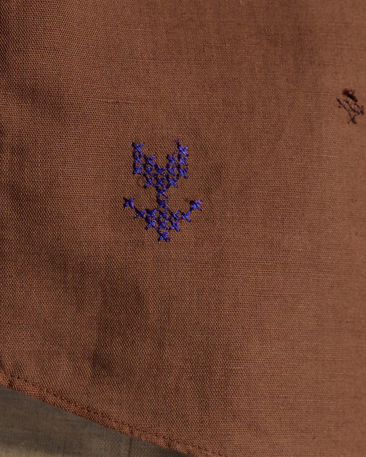Close-up of purple cross-stitch embroidery on a brown Classic Shirt.